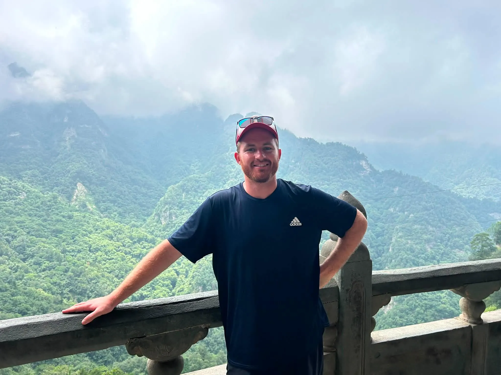 Lewis Samuels smiling, with misty green mountains behind him